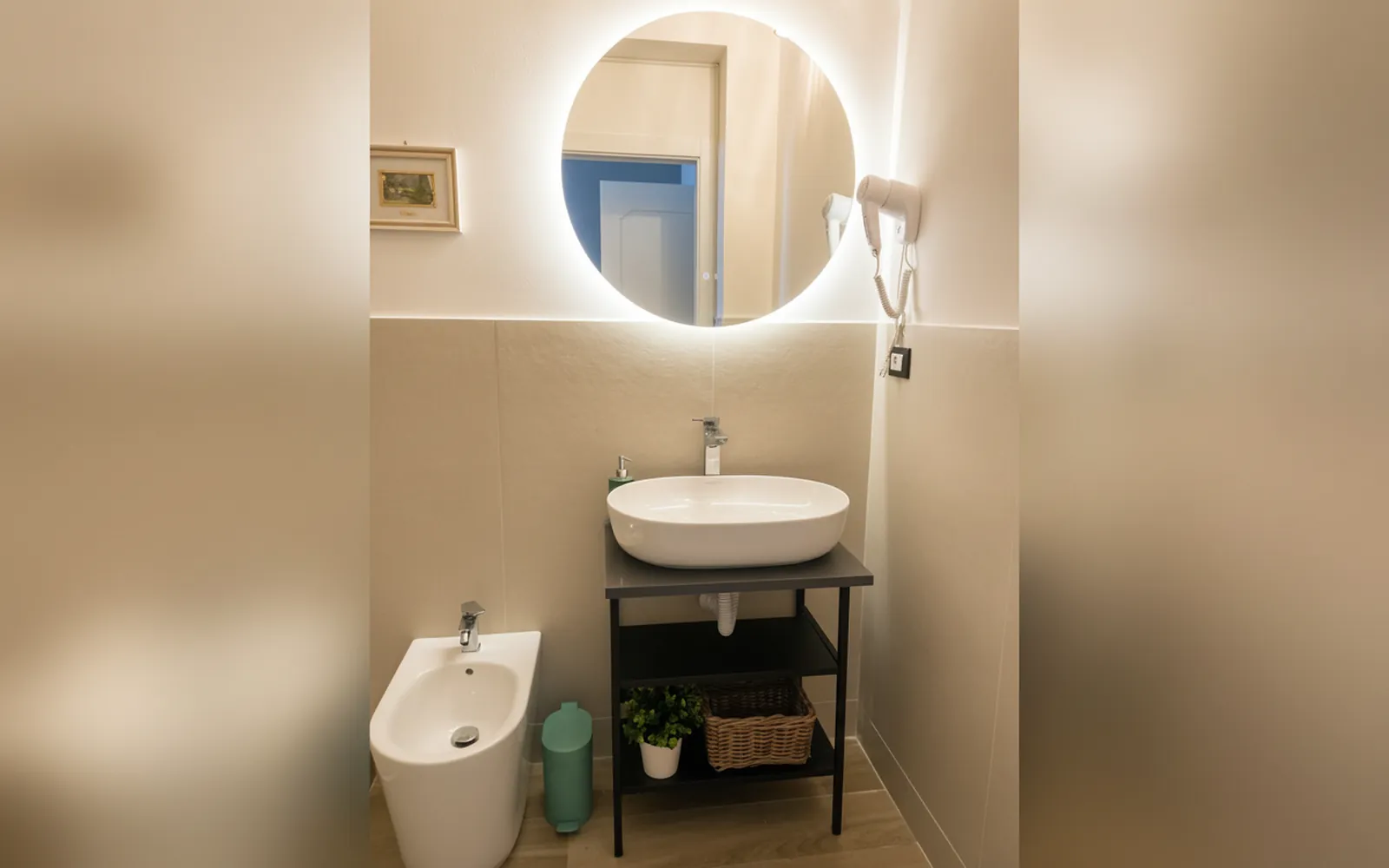 Il bagno privato con lo specchio tondo illuminato, il lavabo e il bidet