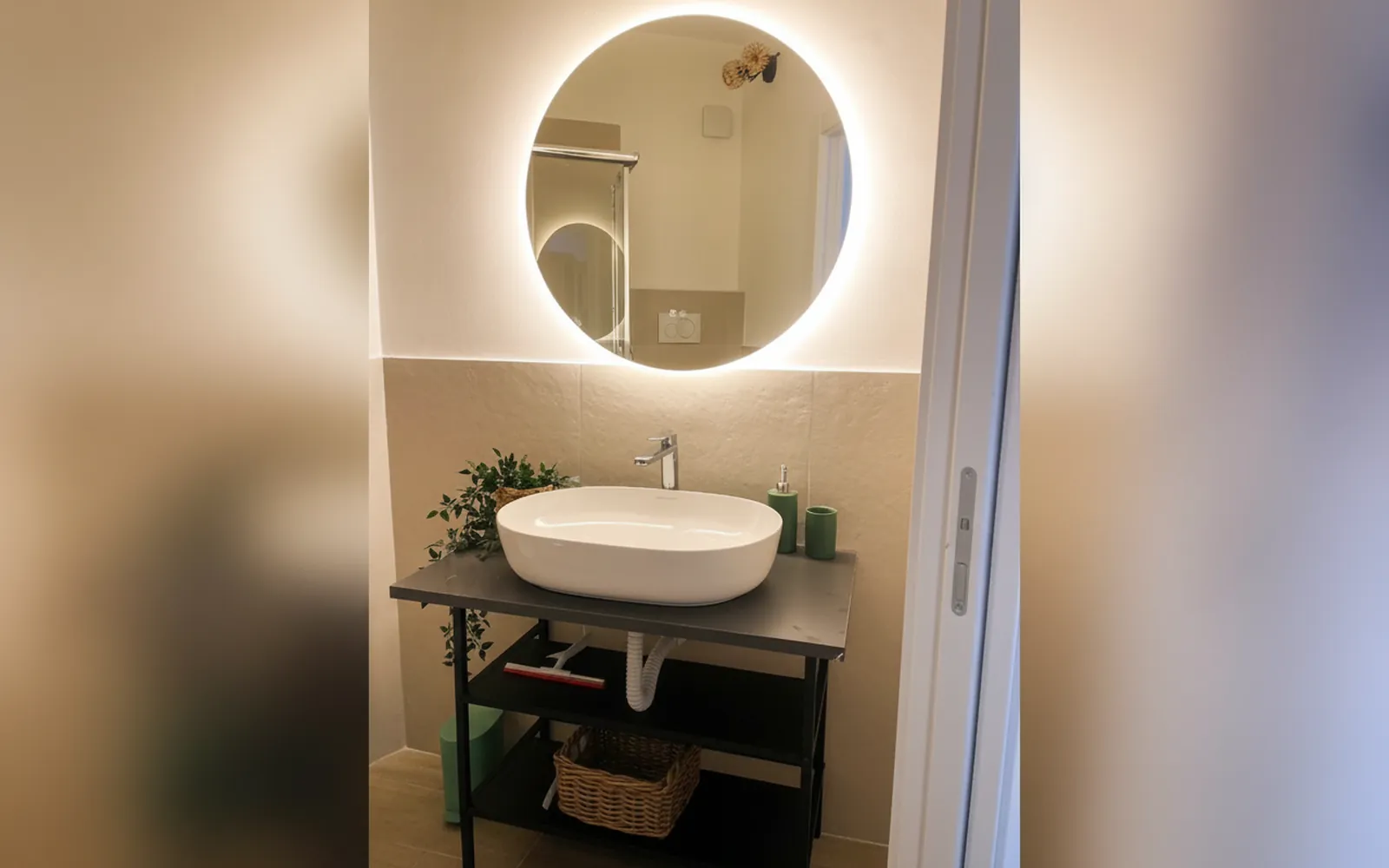 Il bagno privato della camera con lo specchio tondo illuminato e il lavabo